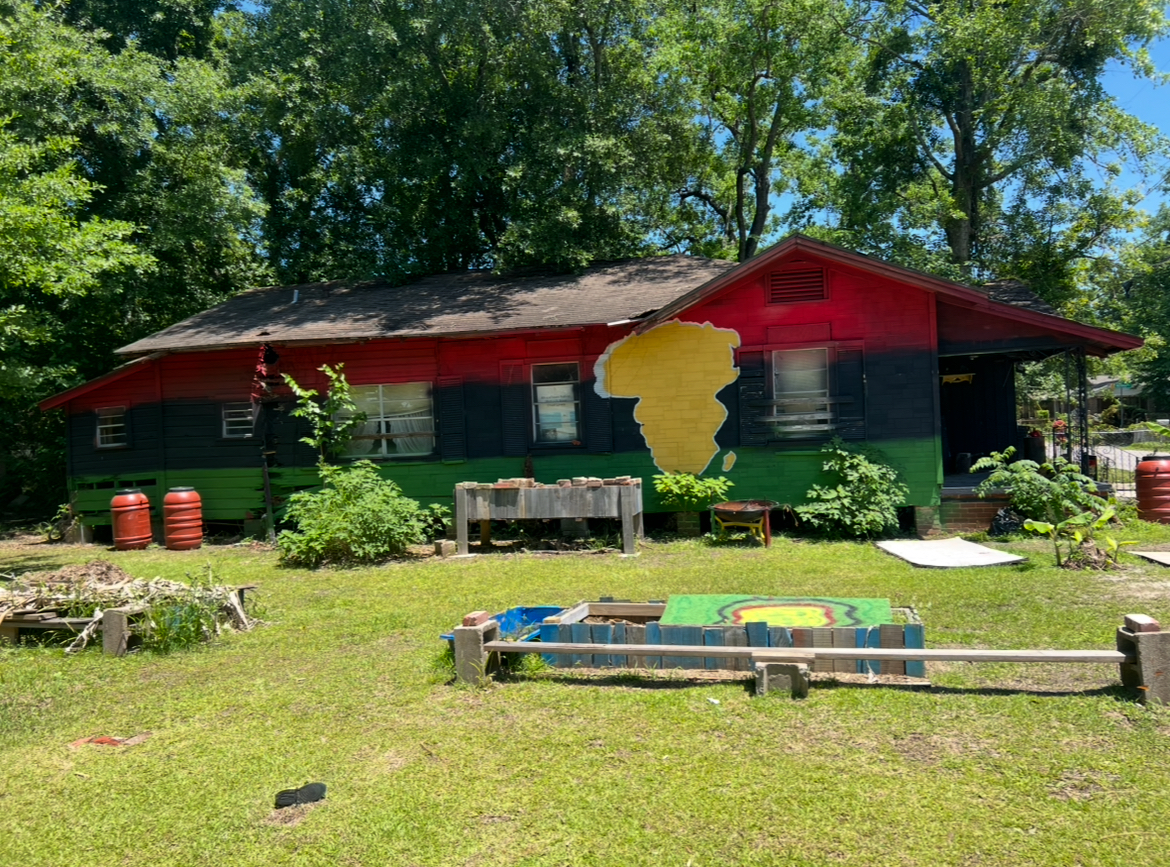 A community house painted in Pan-African red, black, and green with a yellow Africa mural and raised garden beds in front