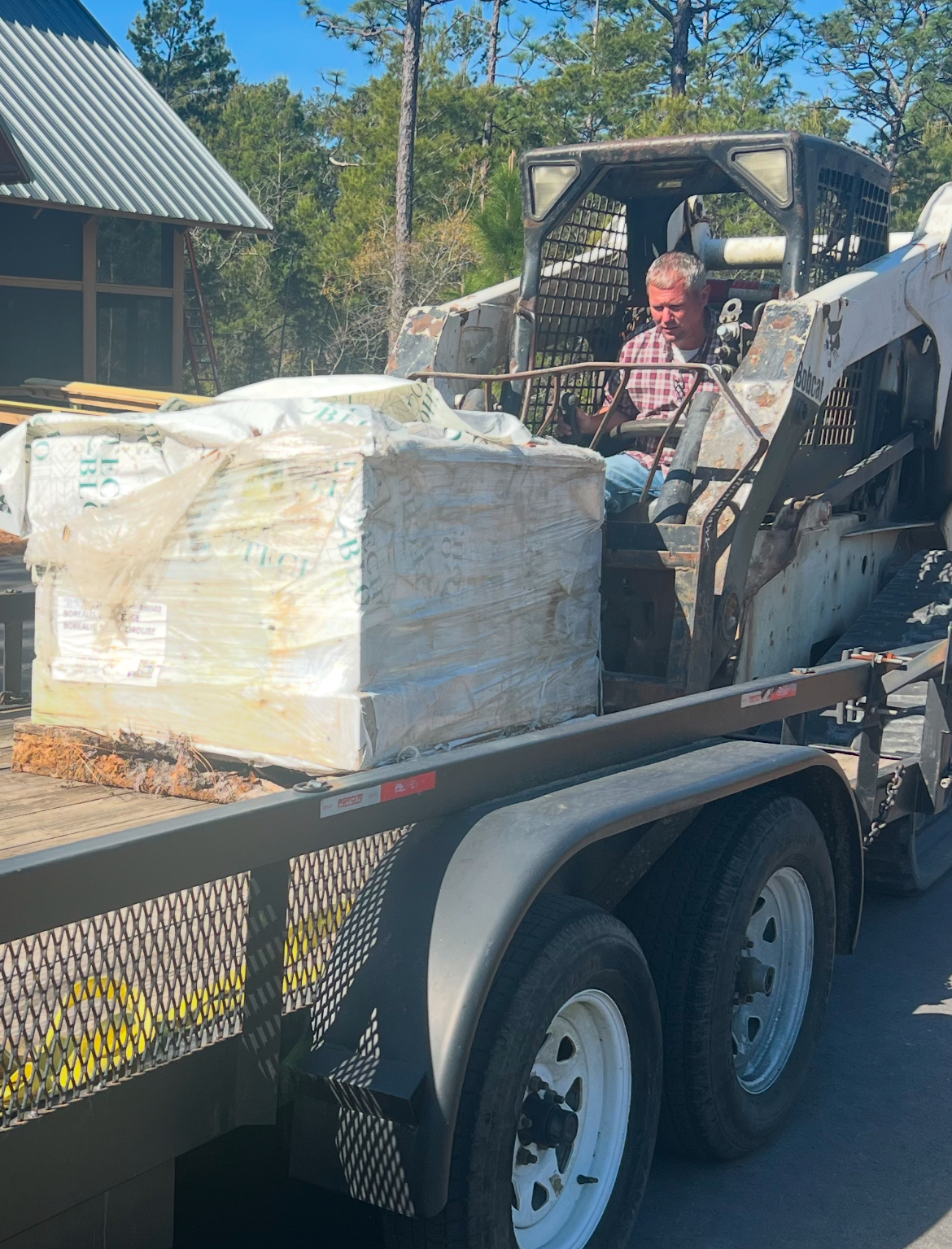 A volunteer operating a Bobcat skid-steer loaded with materials for the raised garden beds