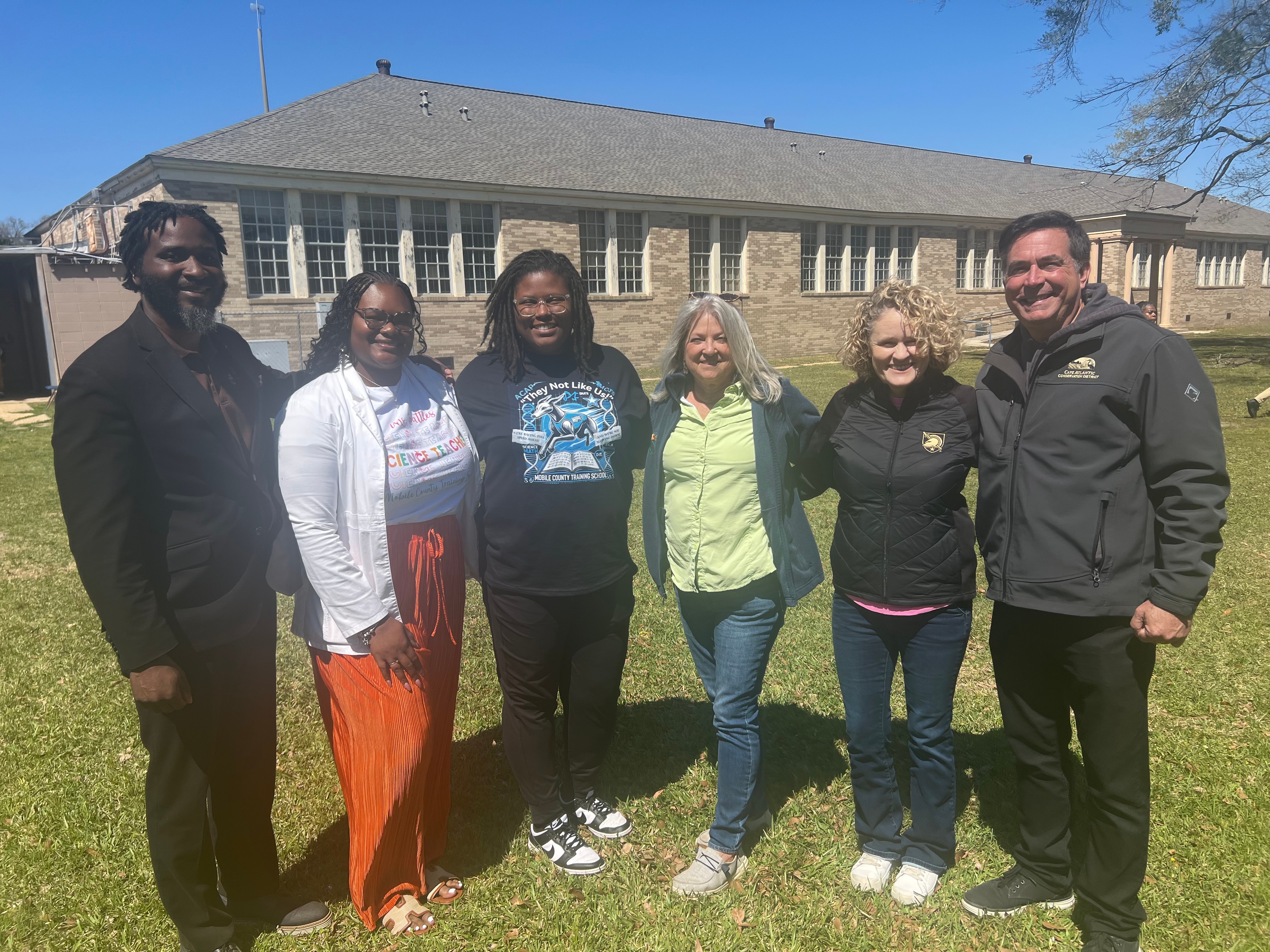 Six community partners and officials standing together in front of the historic Mobile County Training School
