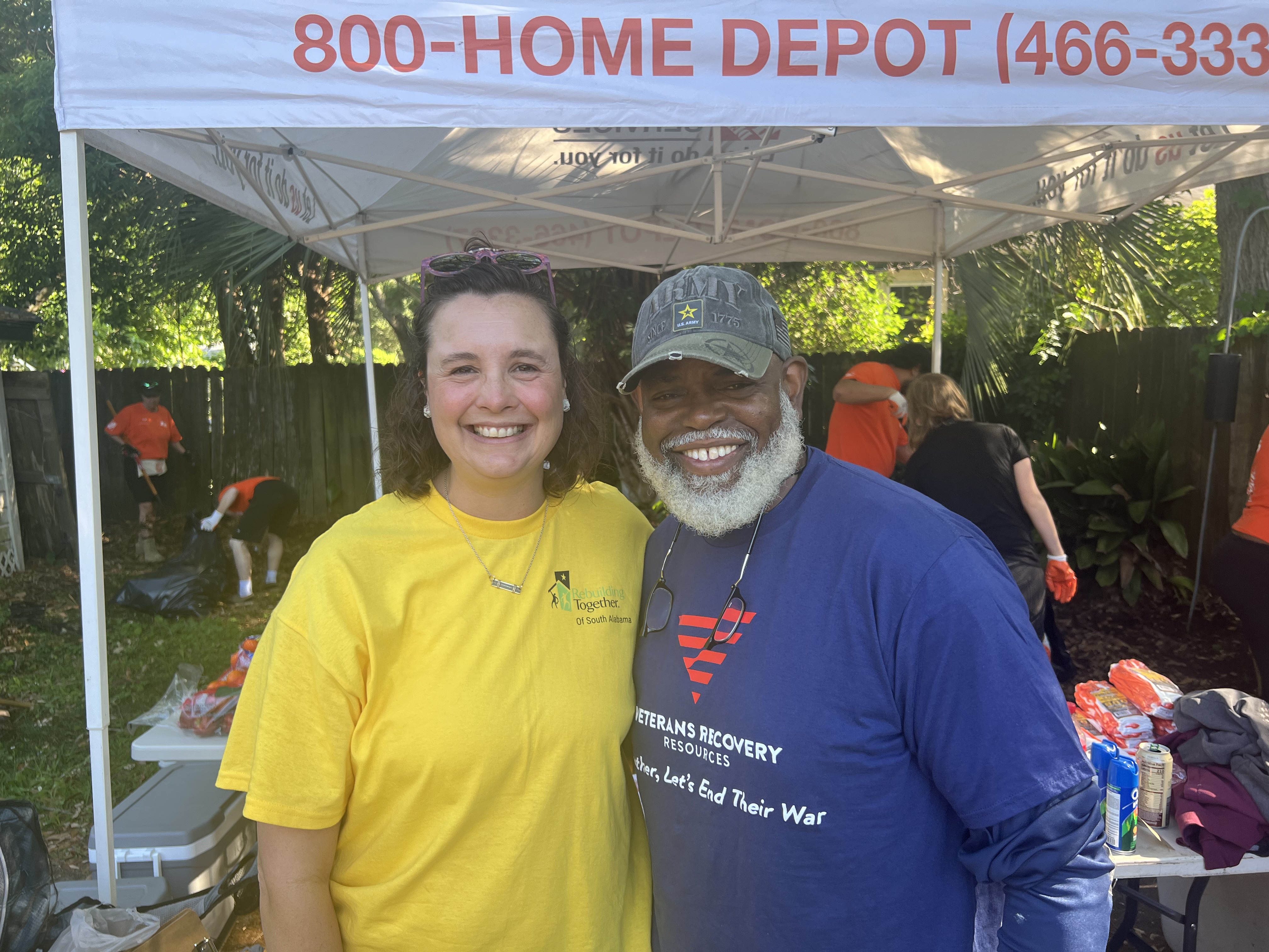 A Rebuilding Together volunteer and a Veterans Recovery Resources veteran smiling together under the Home Depot tent