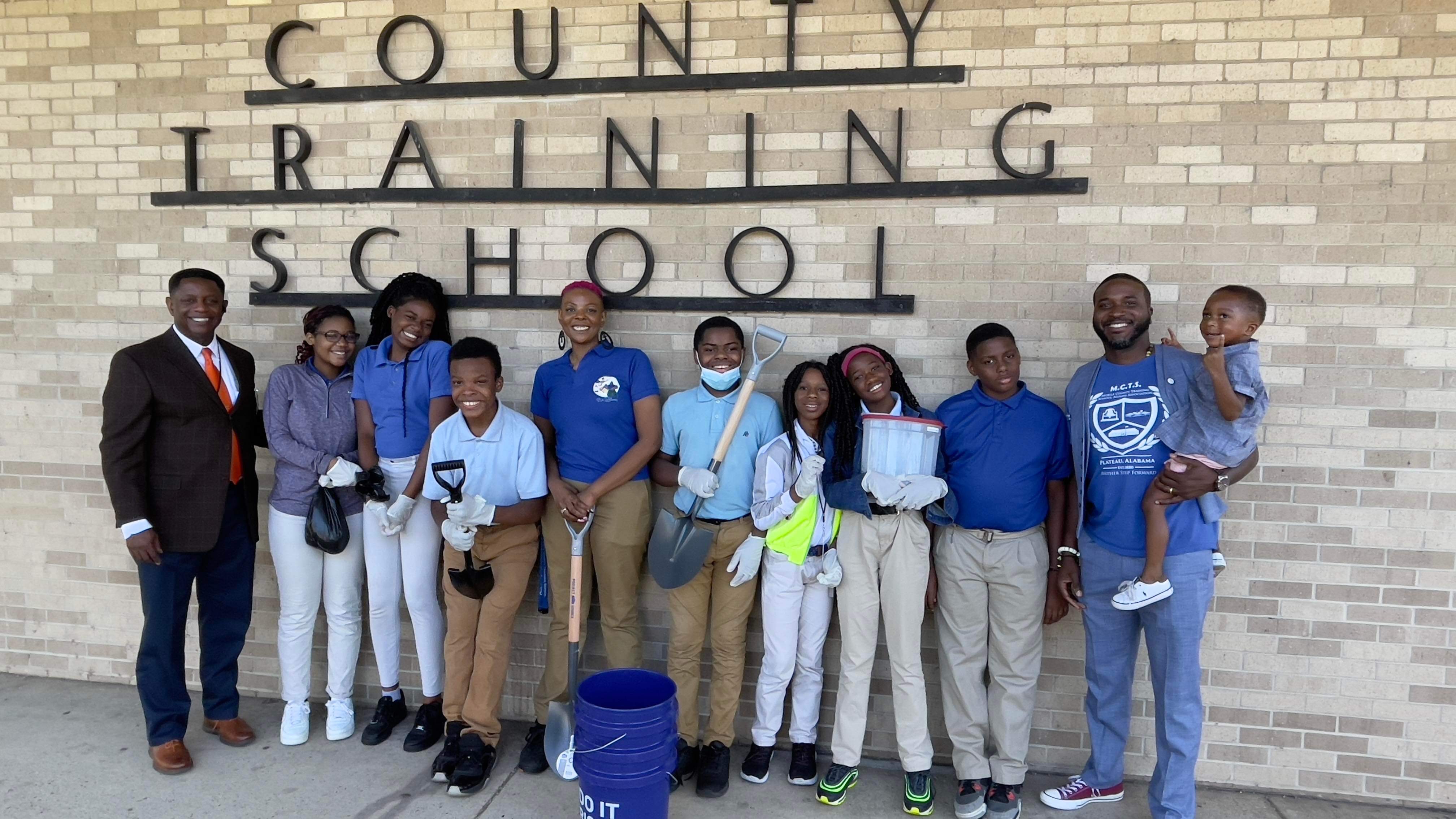 Students and mentors with gardening tools in front of the County Training School