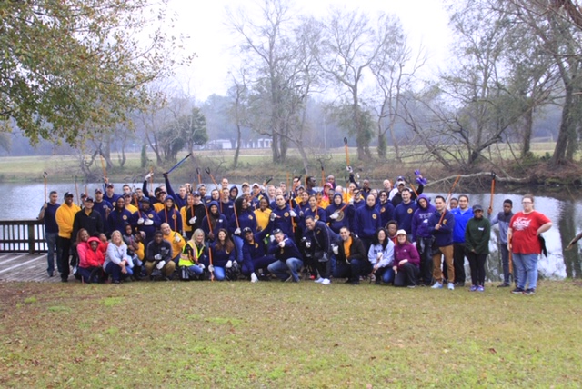 A large group of volunteers with cleanup tools gathered by a lake for an MLK Day of Service event
