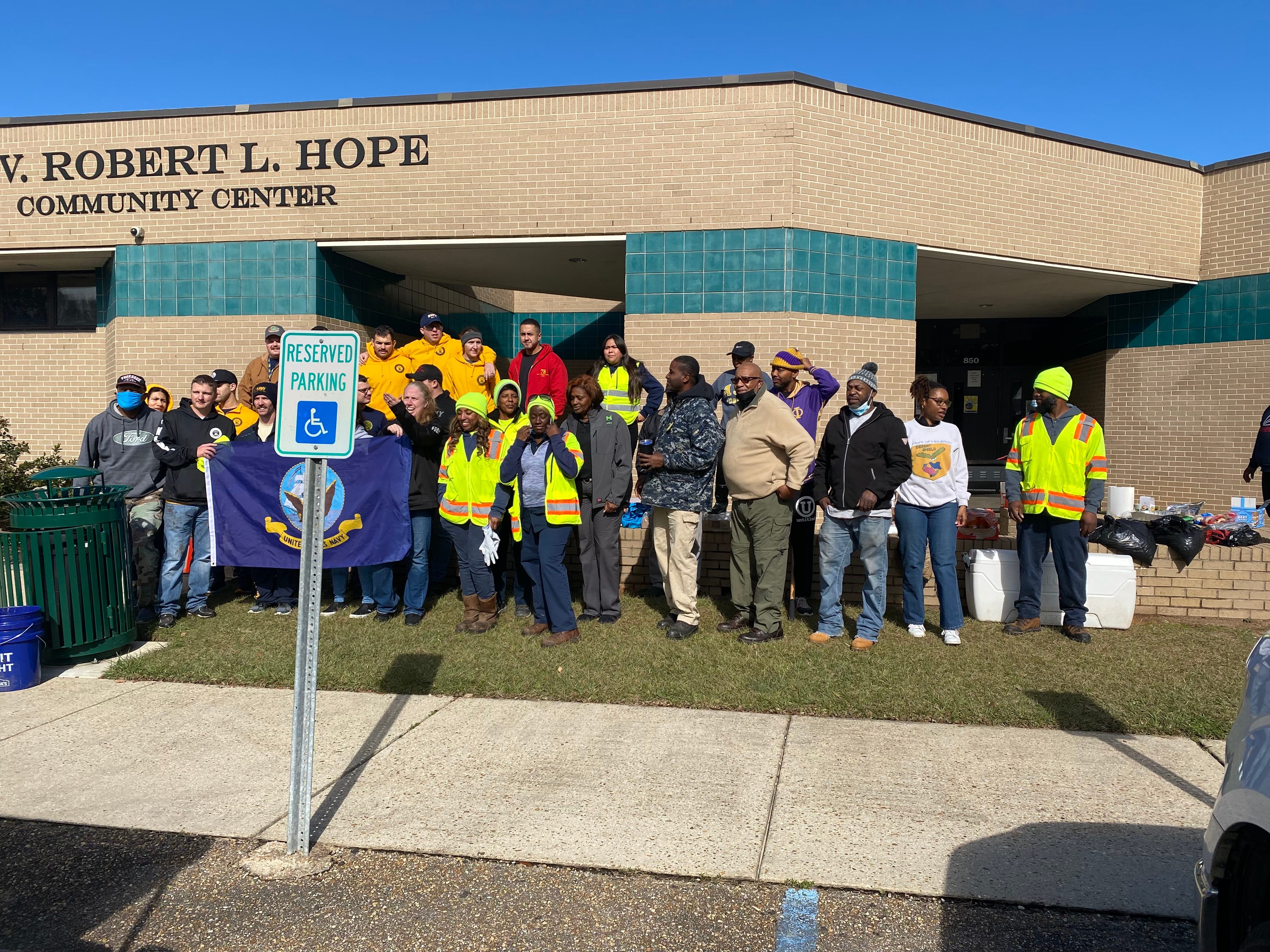 A large volunteer crew holding a U.S. Navy flag outside the Robert L. Hope Community Center